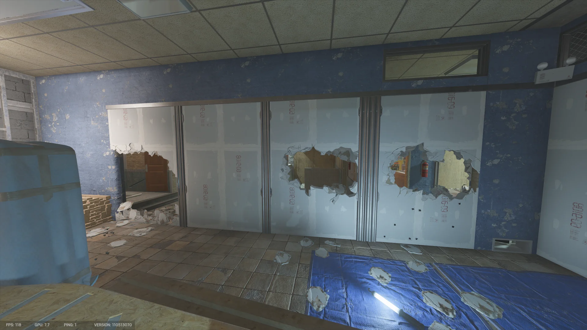 Blue-papered room on Border 1F with a drywall partition breached by three jagged holes, a blue tarp and drywall debris on the tiled floor