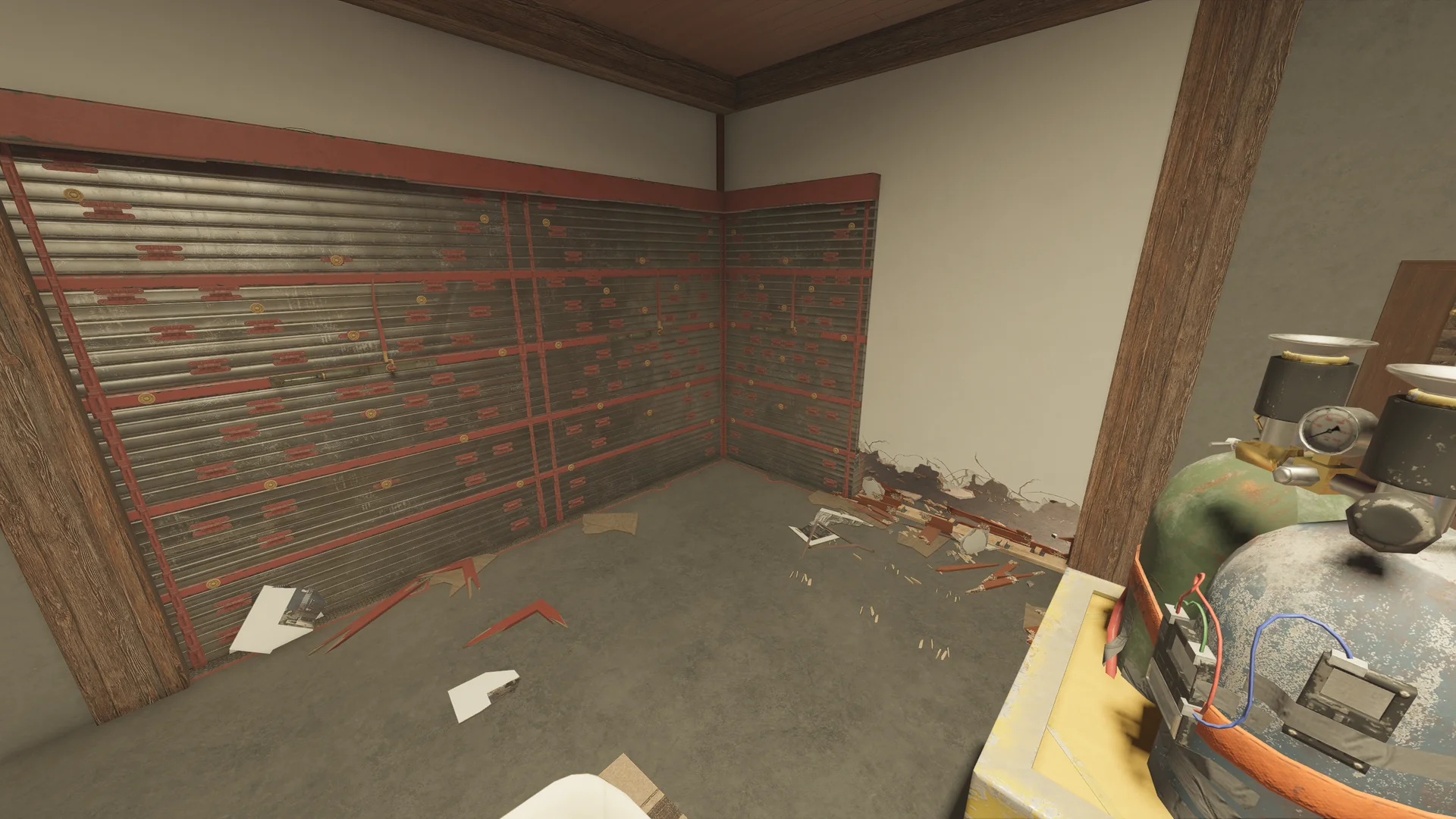 Corner on Chalet 1F with reinforced walls on two sides, gas cylinders with gauges at right and debris on the concrete floor