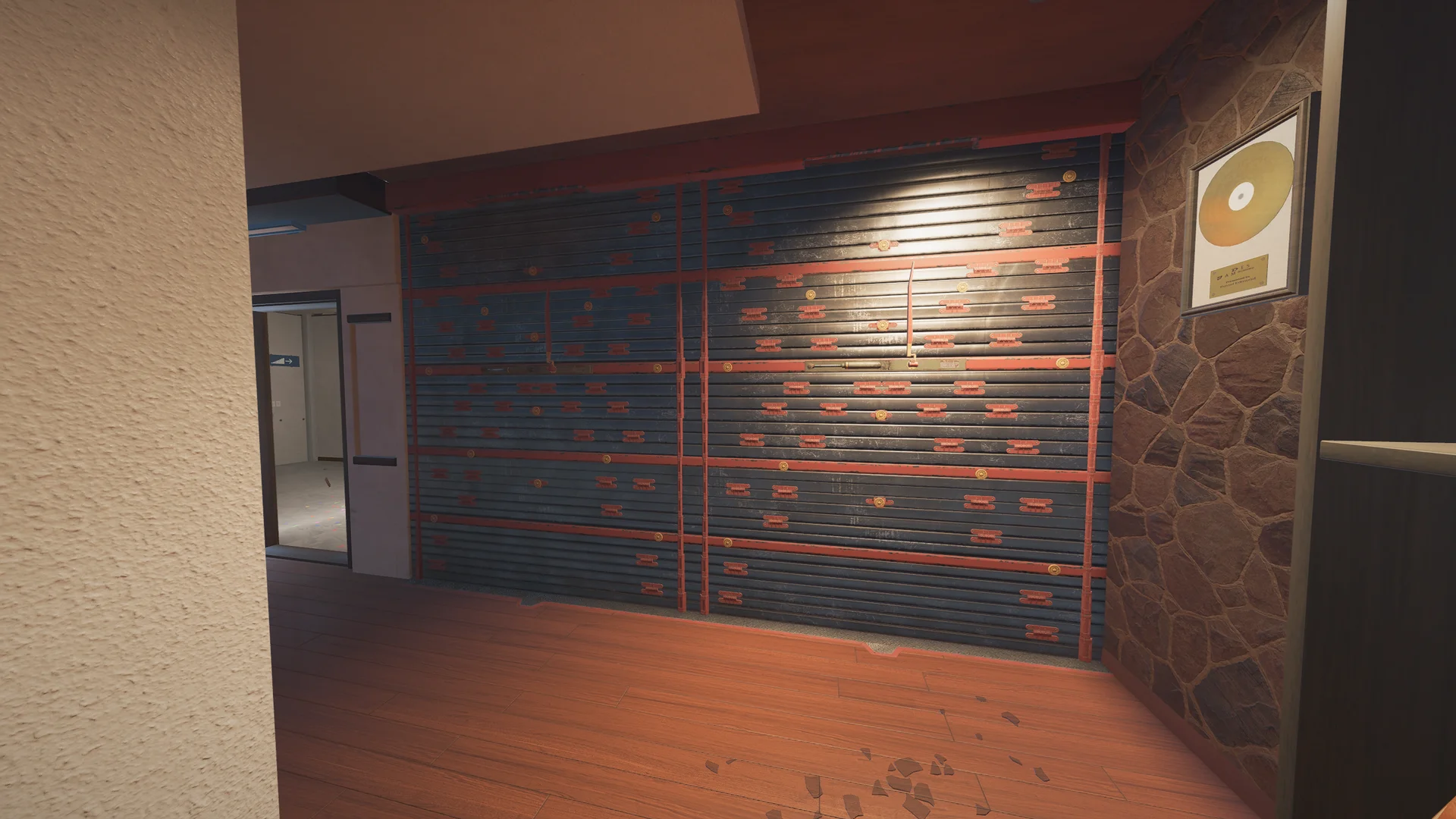 Room on Coastline 2F with a large reinforced shutter wall, a framed gold record on a stone wall, and an open doorway at left