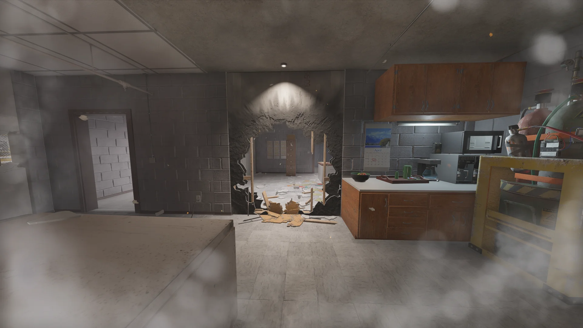 Basement area in the Consulate with a large breach hole punched through a wall, a kitchenette with a microwave, and a doorway at left