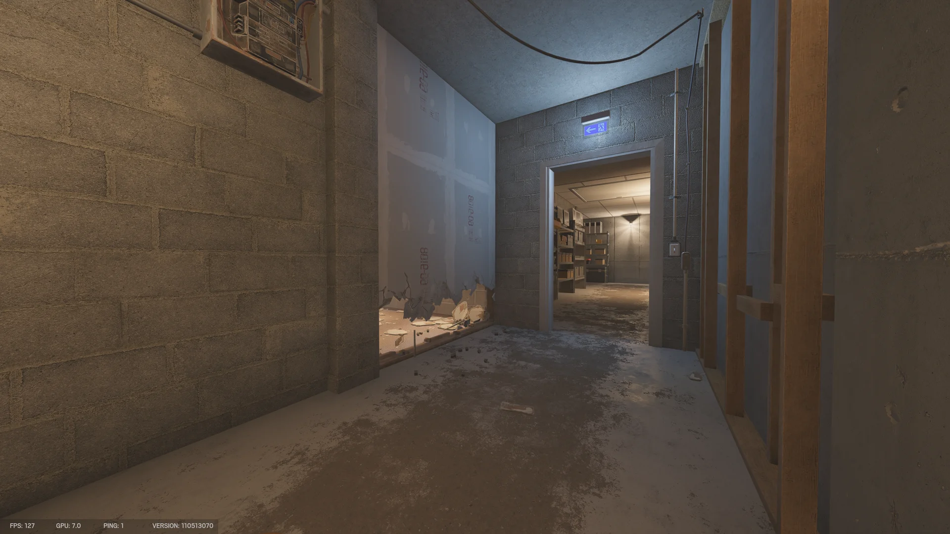 Dim basement corridor in the Consulate with an exit sign, a low breach hole in a drywall wall, and a doorway to a shelved storeroom