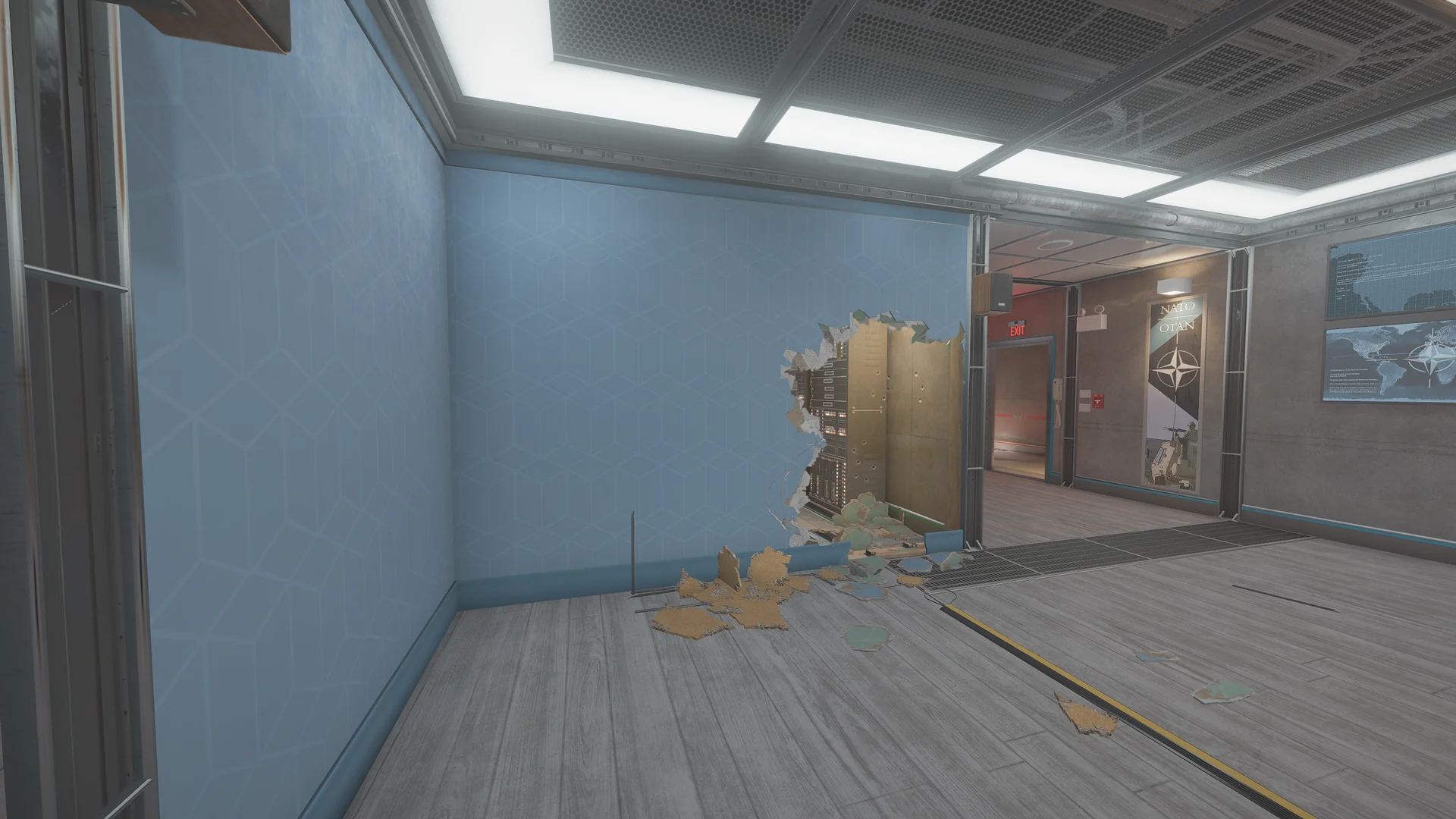 Office on Kanal 2F with a blue patterned wall, a breach hole exposing wiring, a corridor with a NATO banner, and a floor grate